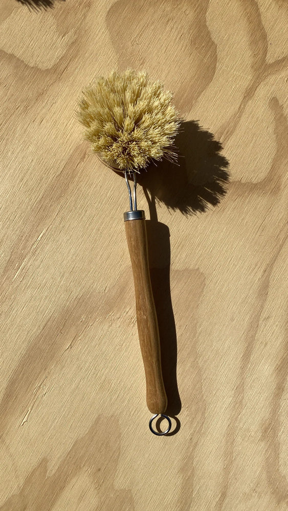 This removable hairbrush has a white teak wood handle and brushhead the stiff Kaveh fibre also vegan made with plant bristles it is held together with silver metal wire and includes a small wire loop at the end for hanging to dry
