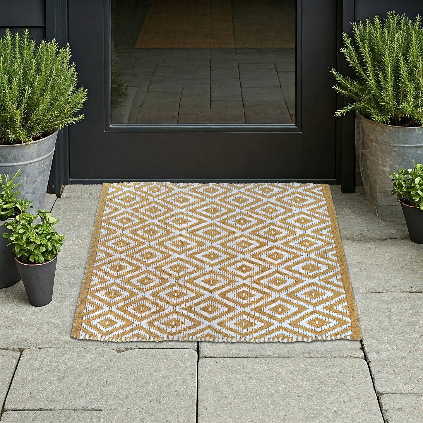 Geometric patterned doormat in front of a black door with potted plants on either side.