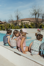 Swimming float vest picture showing 4 kids sitting poolside  all wearing their swim float vest one is wearing a current tyed SnapBack hat as well