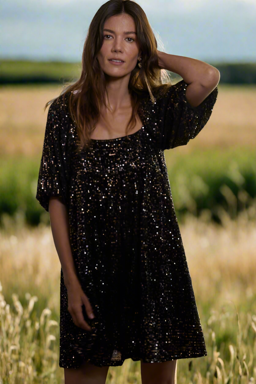 Woman wearing black mini dress sequin puff sleeve low back at country field wedding 