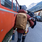 YETI Crossroads 27L Backpack, front view of bag worn on the back of an adult holding a small child walking beside a bus in a mountain town 