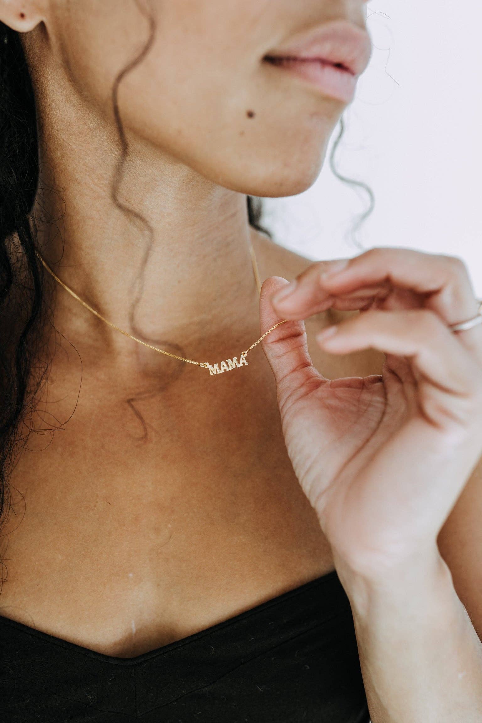 Person wearing a gold 'MAMA' necklace with a blurred background