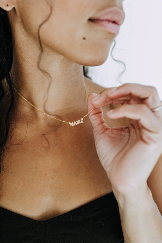 Person wearing a gold 'MAMA' necklace with a blurred background