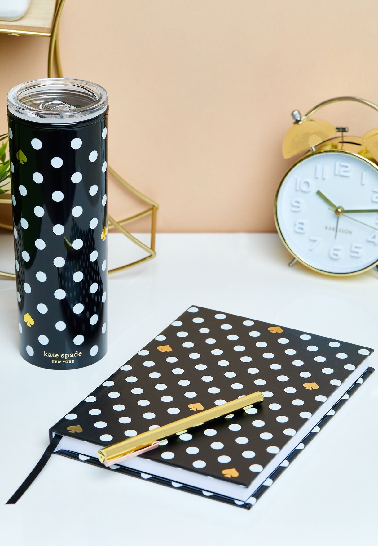Black polka dot tumbler and notebook with a pencil on a white surface, with a clock in the background.